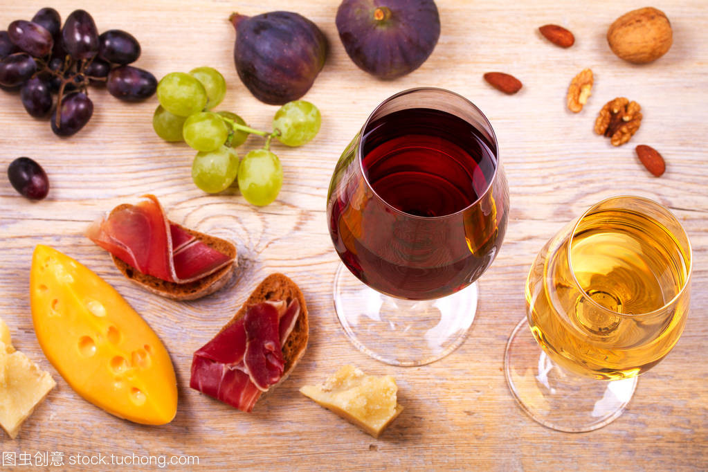 紅色和白色奶酪、 火腿、 無花果和葡萄與葡萄酒杯。木制的桌子上的酒杯。葡萄酒的靜物